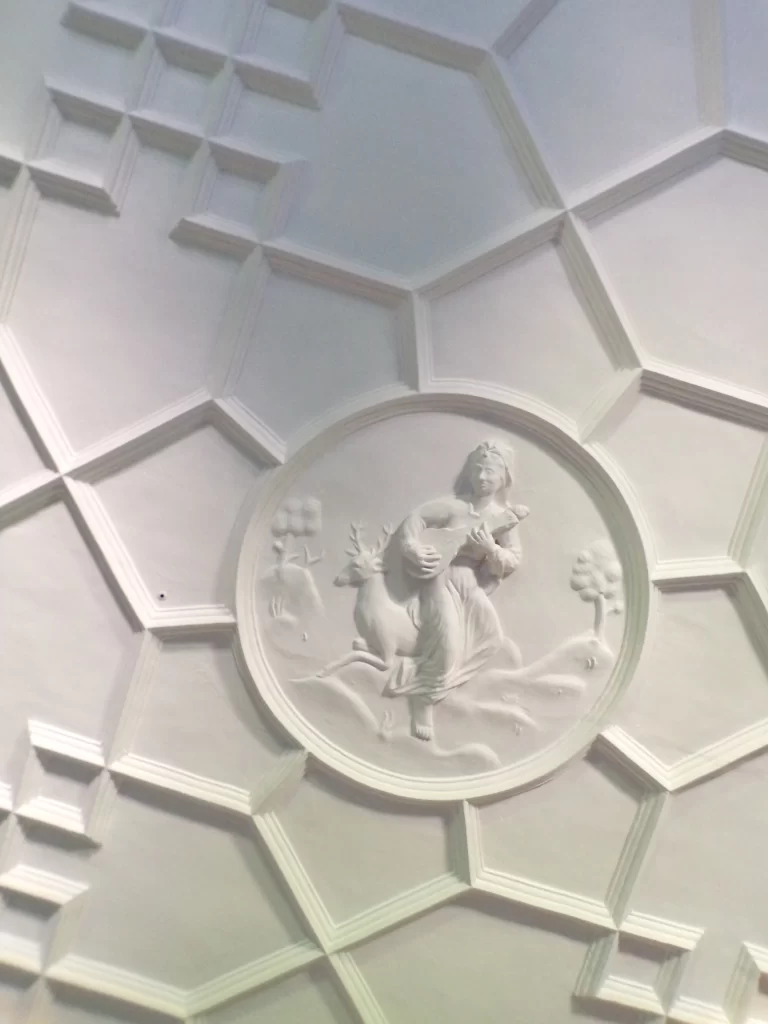 A ceiling decorated with the five human senses. Pictured is 'hearing' or 'listening' depicted through a person playing a musical instrument